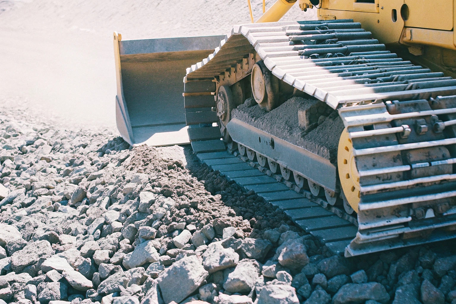 Close-up of yellow bulldozer tracks pushing gray rocks on a construction site.
