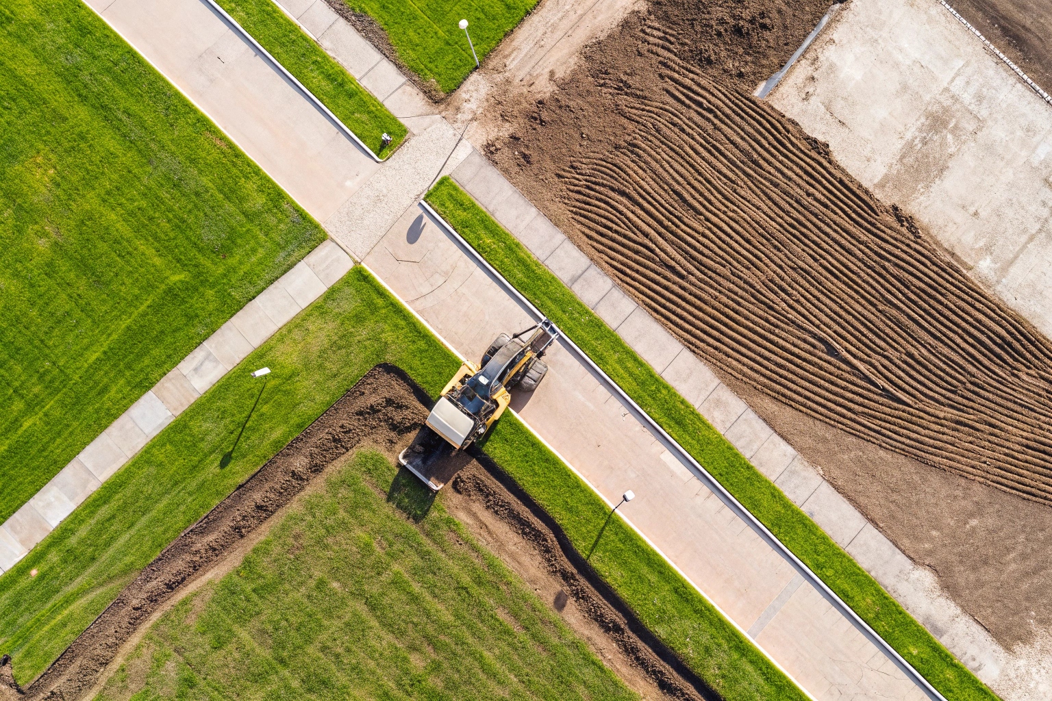 Aerial view of construction vehicle landscaping new development with grass and paths.